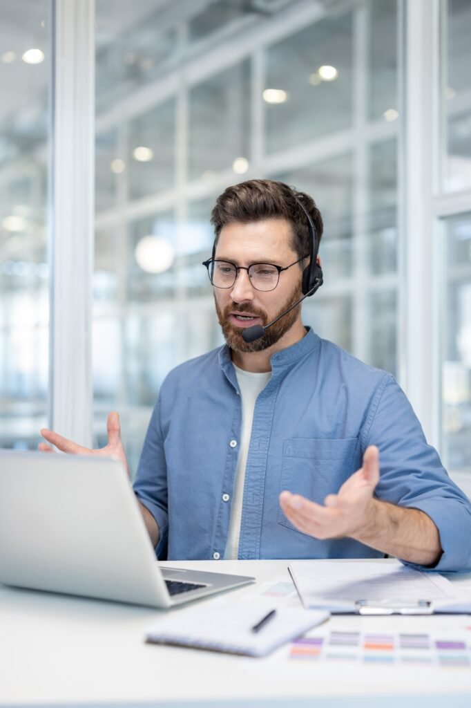 Vertical shot, man with headset talking and consulting customers remotely at workplace. Serious and